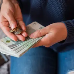 Dłonie trzymające stos banknotów i monet.